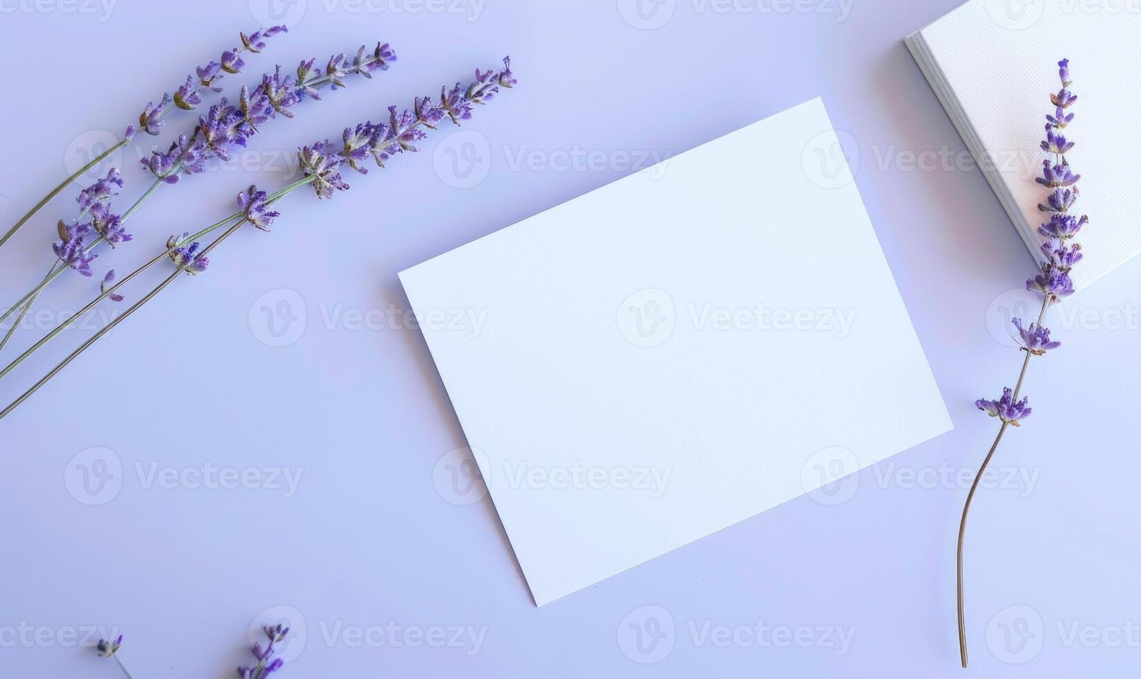 White blank card on a pastel periwinkle table, with a sprig of lavender and a small notebook photo