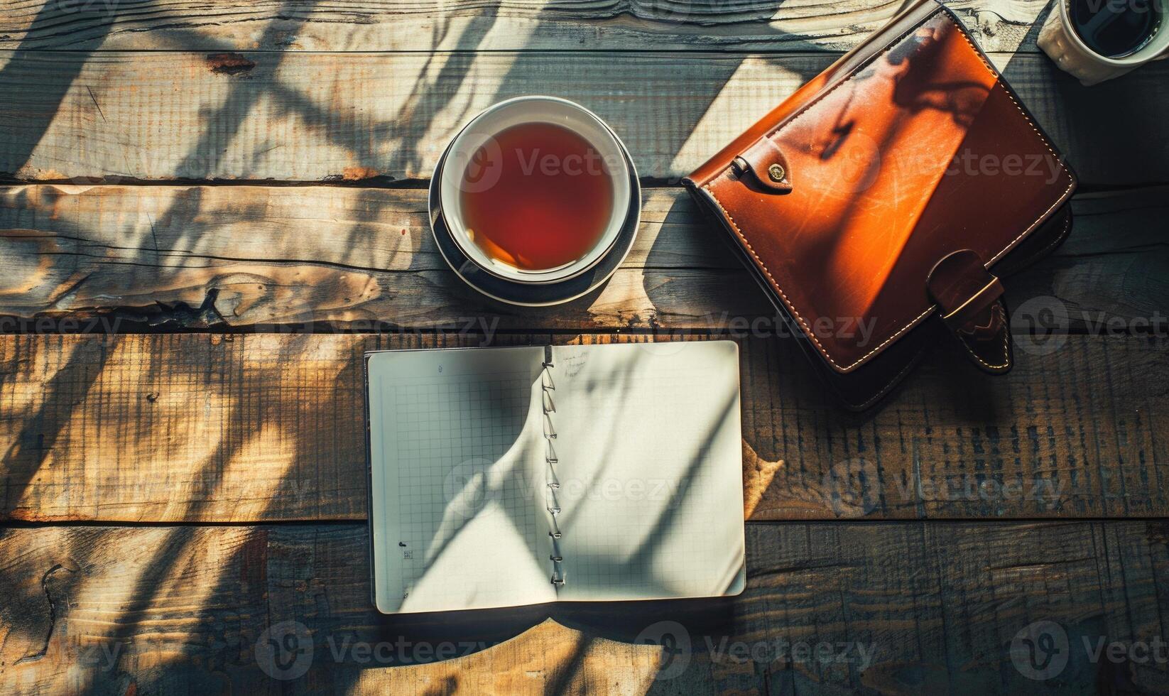 Notebook on a wooden table with a cup of tea and a handbag photo