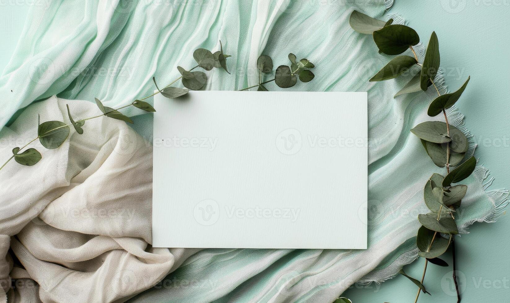 White blank card on a pastel mint green table, with a sprig of eucalyptus and a linen cloth photo