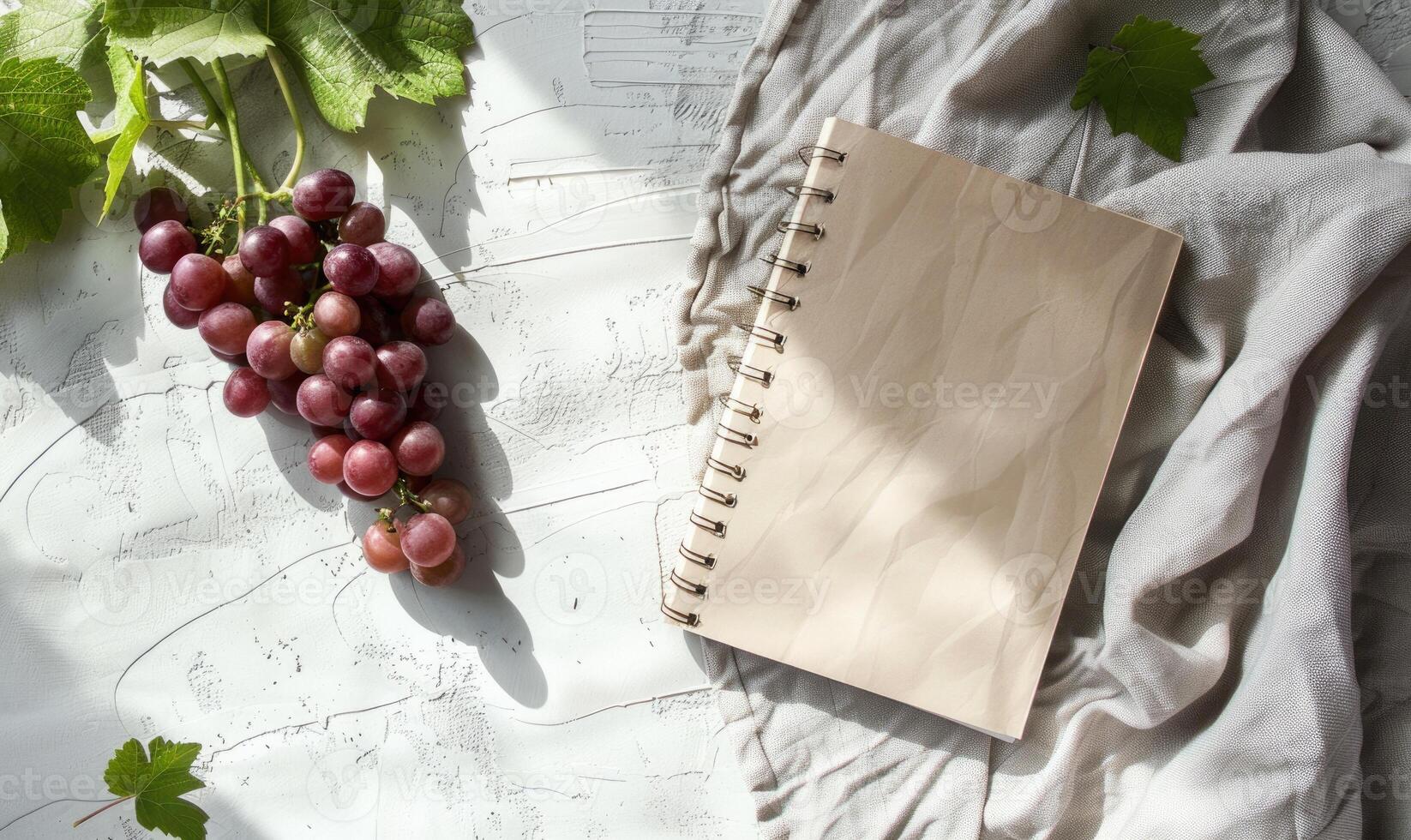 Closed notebook on a light gray table with a bunch of grapes photo