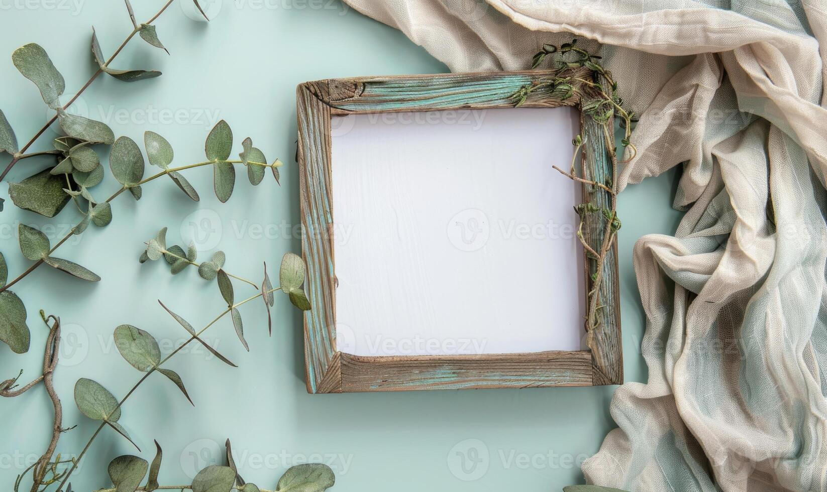 White blank card in a rustic wooden frame on a pastel mint green table, with a sprig of eucalyptus and a linen cloth photo