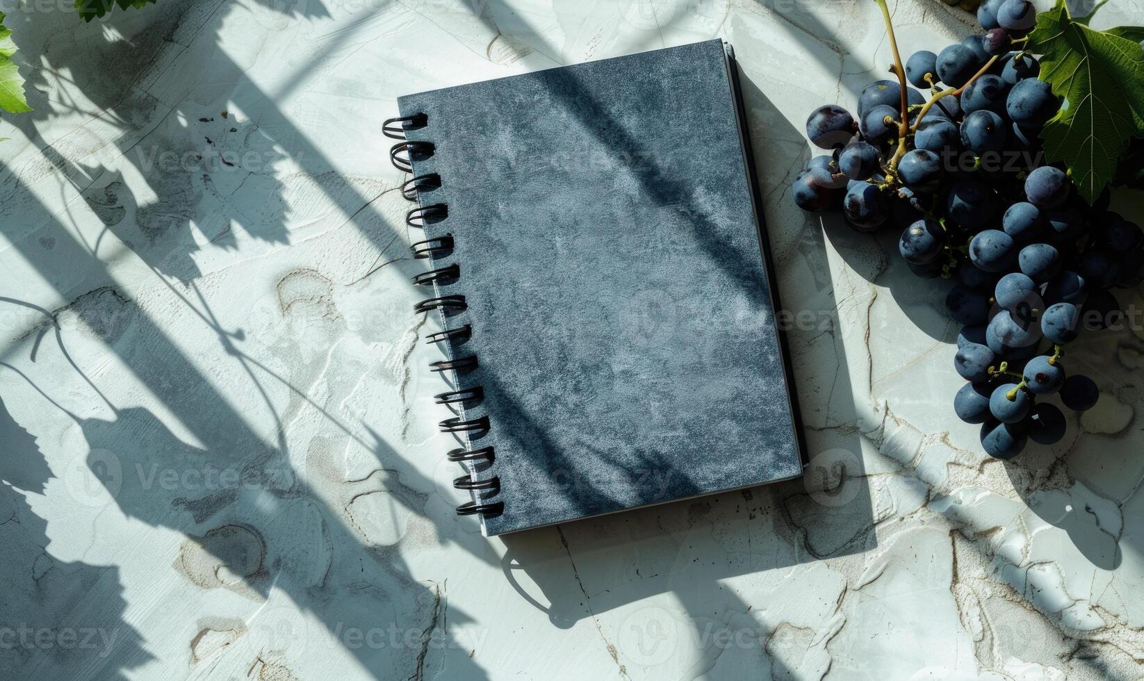 Closed notebook on a light gray table with a bunch of grapes photo
