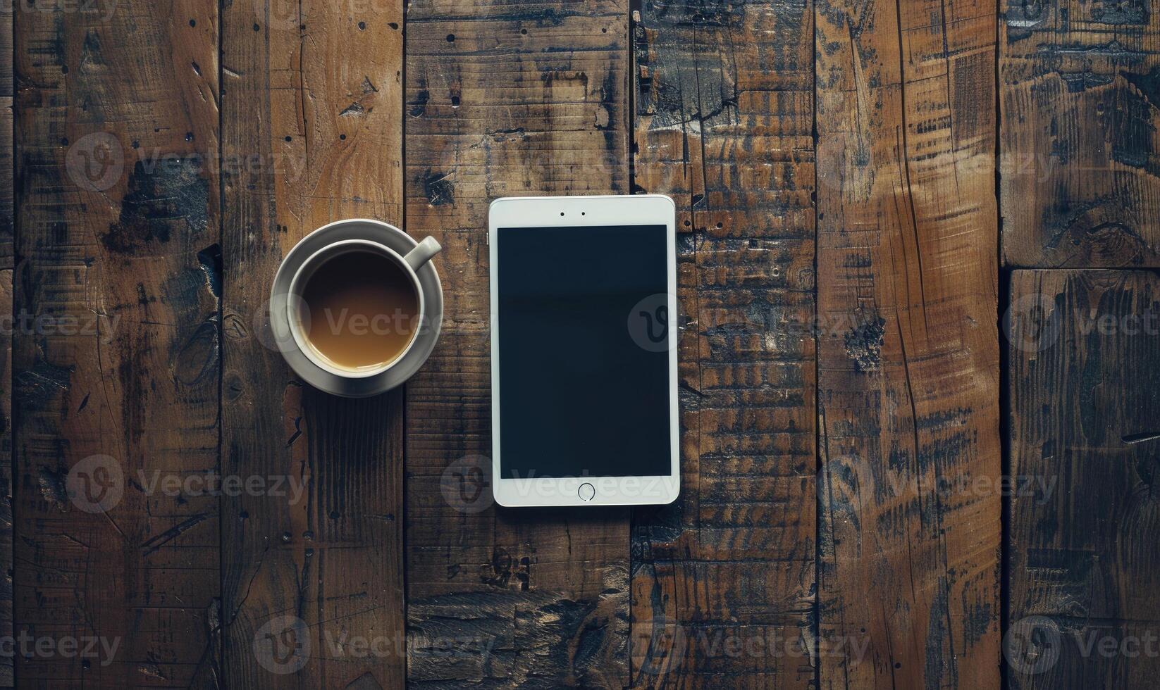 Tablet on a wooden table with a cup of coffee on the left photo