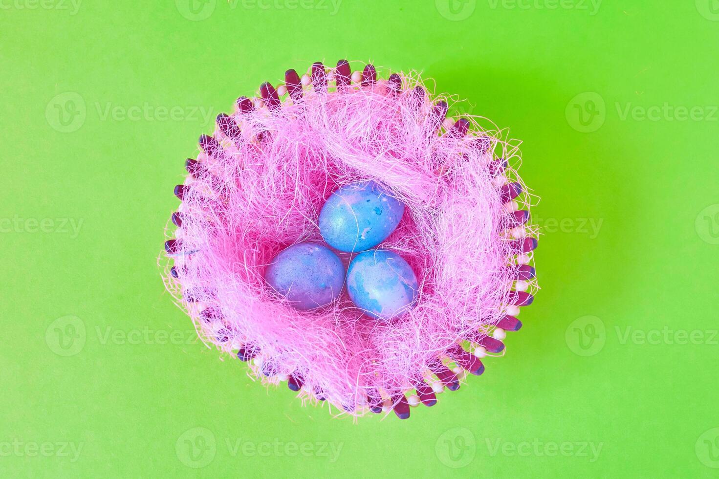 Three Easter eggs with space galactic pattern in a basket with a filler in the form of a pink nest on a green background. flat lay photo