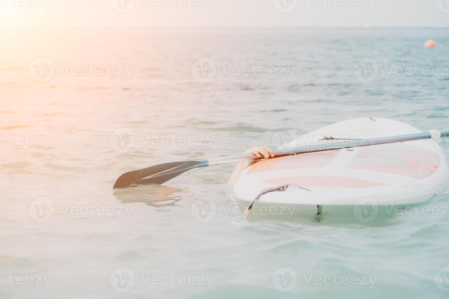 Sea woman sup. Silhouette of happy young woman in pink bikini, surfing on SUP board, confident paddling through water surface. Idyllic sunset. Active lifestyle at sea or river. photo