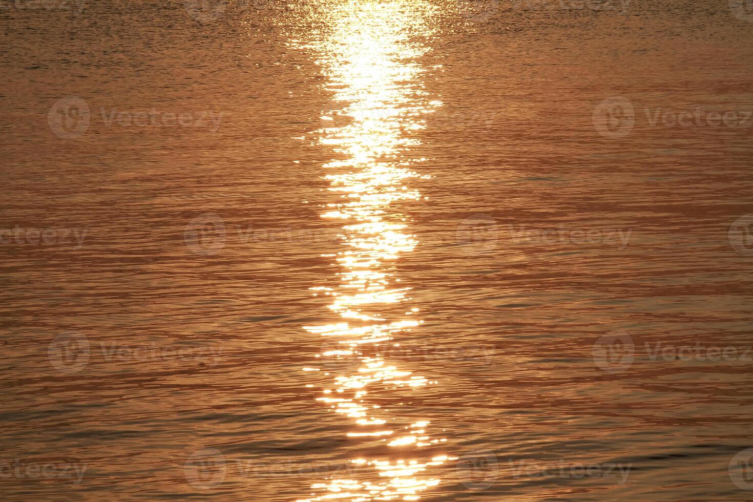 Calm ocean waves with golden light reflections from the rising sun photo