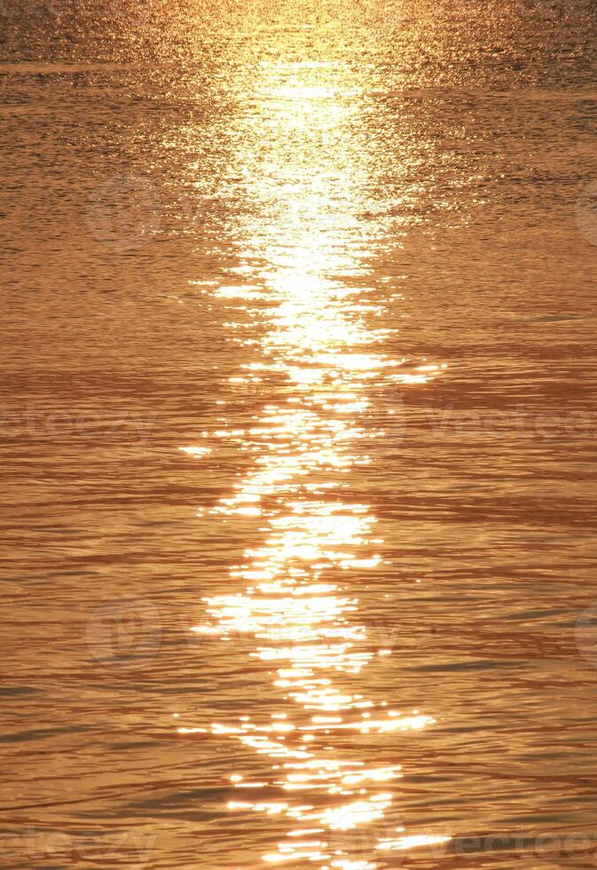 Calm ocean waves with golden light reflections from the rising sun photo