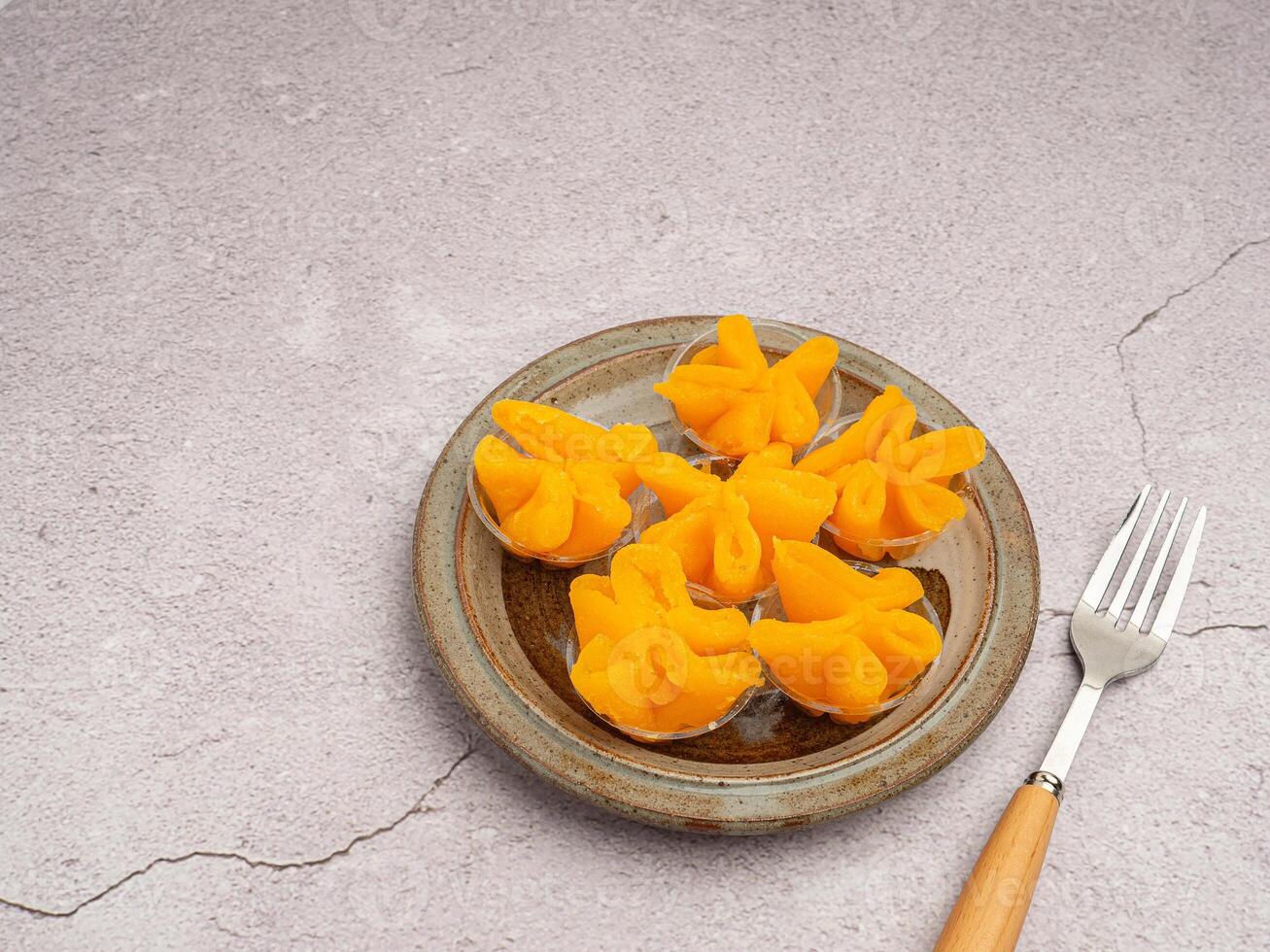 Pinched Gold Egg Yolks or Khanom Thong Yip in the Thai language are placed on a plate with cutlery and cloth placed nearby on gray stone background. Thai dessert photo