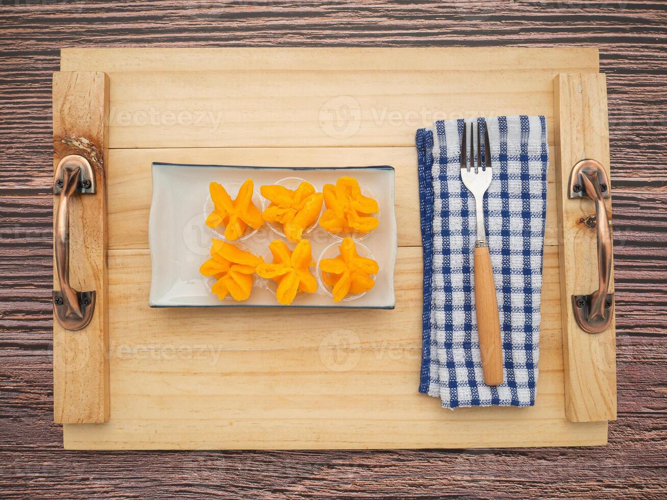 Pinched Gold Egg Yolks or Khanom Thong Yip in the Thai language are placed on a plate with cutlery and cloth placed nearby on a wooden tray background. Concept of Thai dessert photo