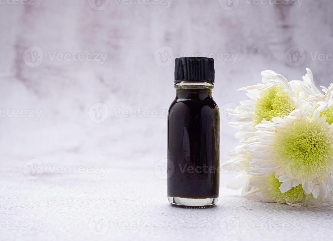 The essential oil in a bottle and flowers placed on a gray stone background. Space for text. Side view photo