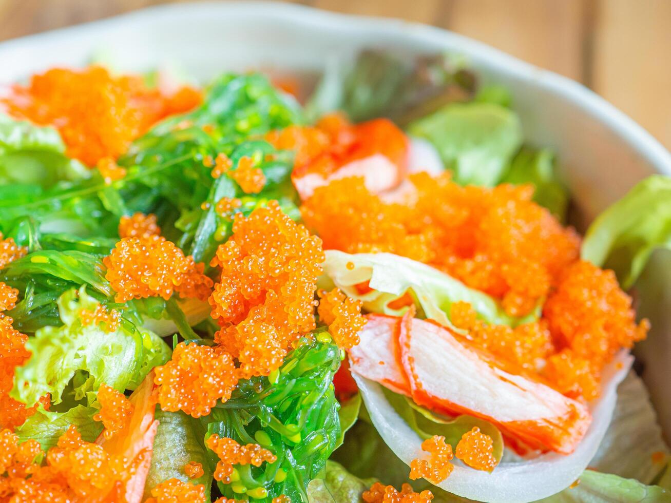 Japanese salad shrimp roe, crab sticks, and seaweed in a bowl placed on a wooden table. Close-up photo. Top view with copy space for text. Concept of healthy foods and vegetables photo