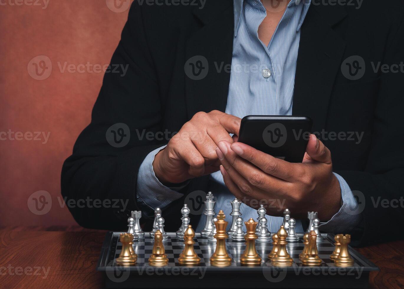 Businessman using a smartphone with the chessboard placed on a wooden table while sitting in the office. The decision on the game. Concept of business, strategy, communication, and planning photo