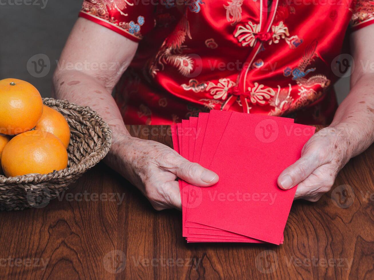 Hands of a senior woman holding red envelopes or Angpao wearing a traditional cheongsam qipao dress while sitting in the studio. Chinese New Year photo