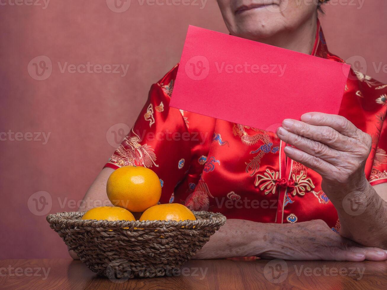 Hands of a senior woman holding red envelopes or Ang Pao wearing a traditional cheongsam qipao dress while sitting in the studio. Chinese New Year photo