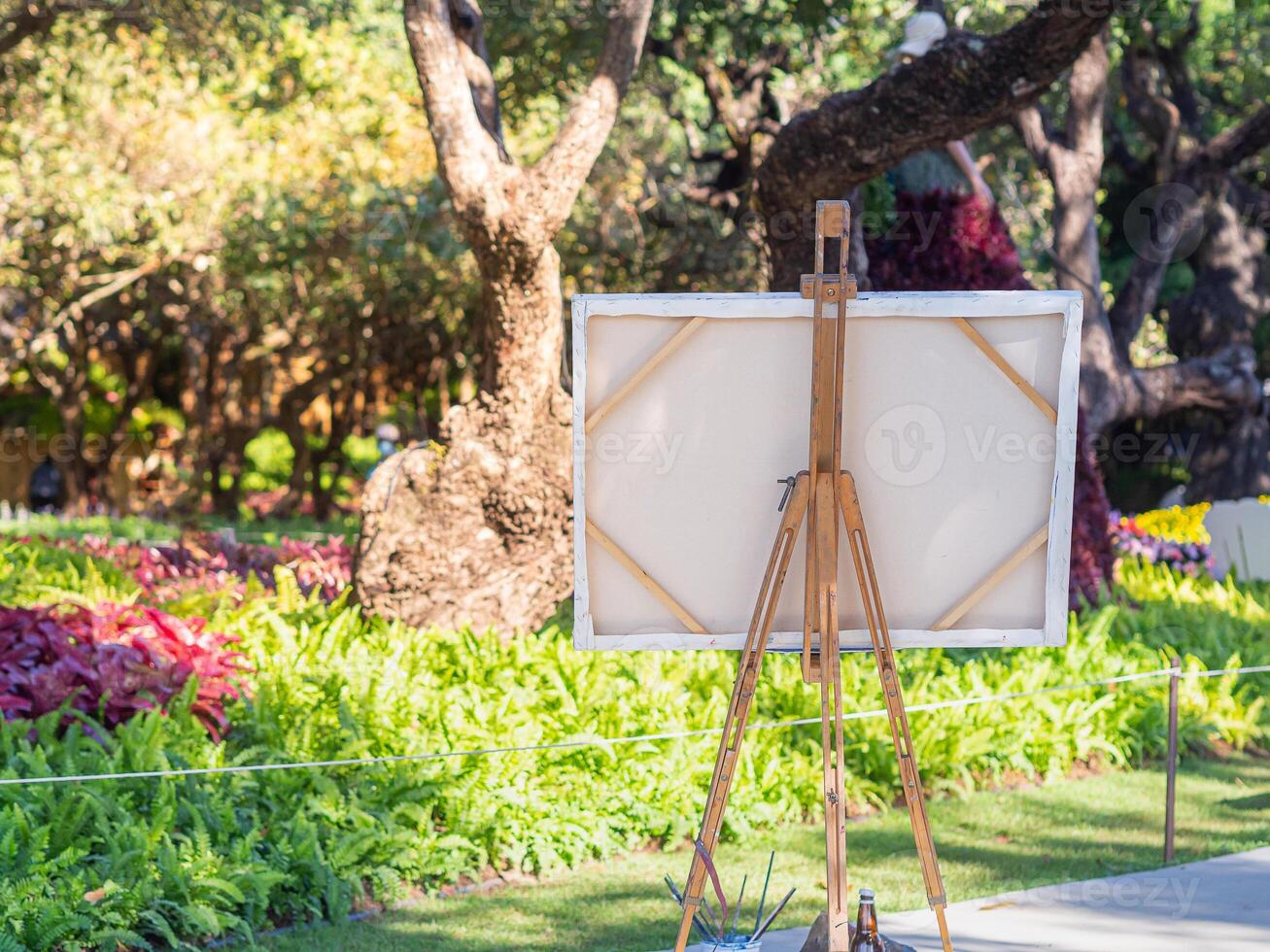 Back view of a wooden easel with white canvas in the park. Drawing easel. Copy space for your text. Concept of art and drawing photo