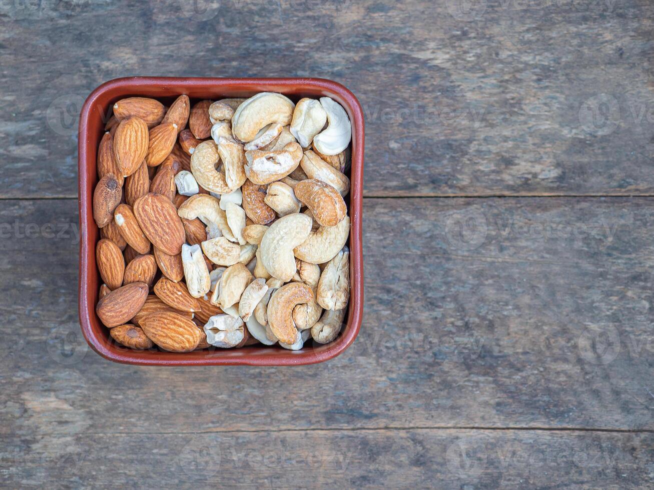 Almonds and cashew nuts in a brown bowl on a wooden table. Top view. Space for text. Concept of healthy fruit and snack photo