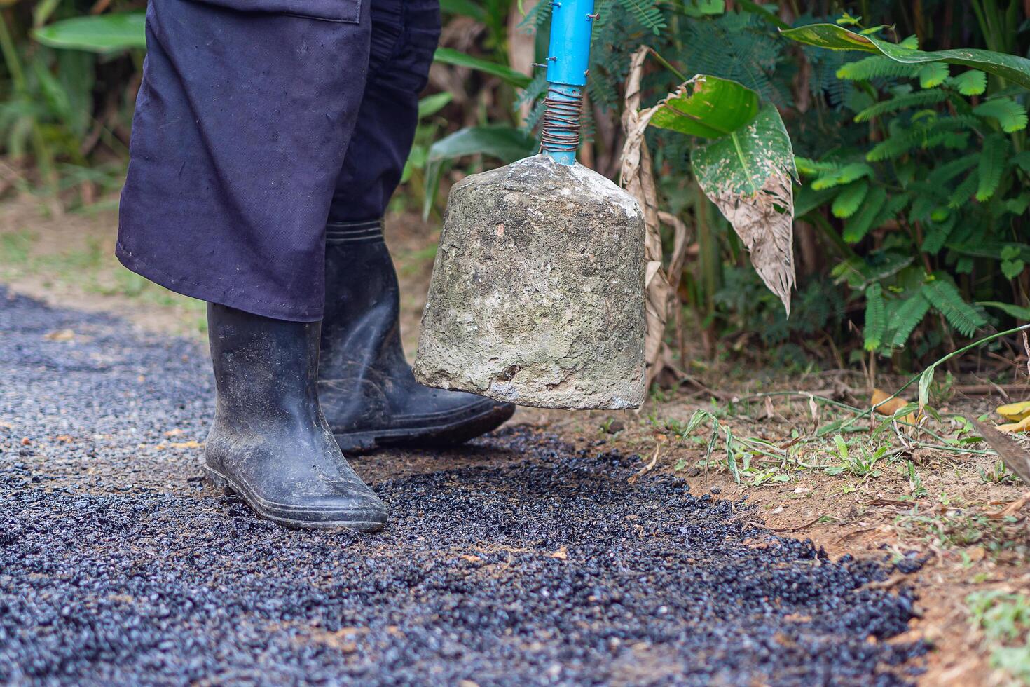 Man holding a cement rod for hammering to adjust the asphalt surface for the walkway. Close-up photo. Constructed from asphalt. Space for text photo