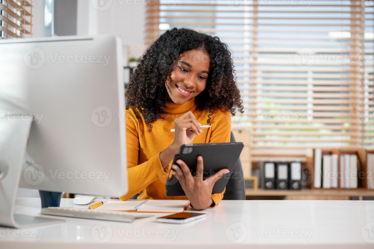 An attractive, positive Black businesswoman using her digital tablet at her desk in the office. photo