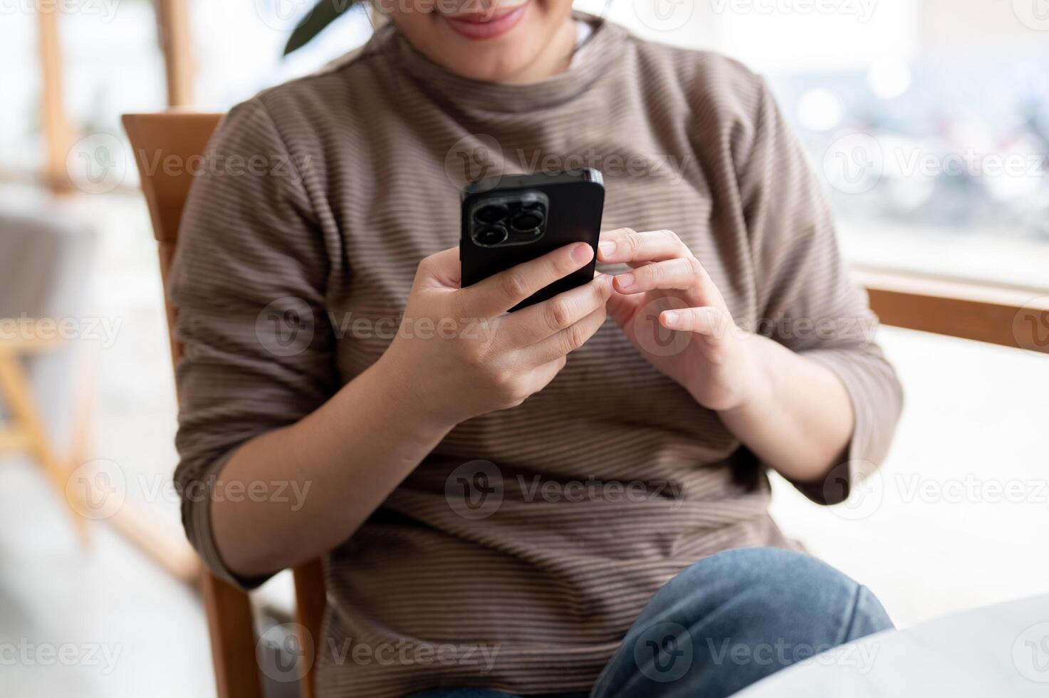 A cropped image of an Asian woman in casual clothes is using her smartphone while chilling in a cafe photo