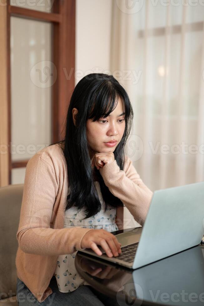 A serious, thoughtful Asian woman is focusing on working on her laptop computer, at a coffee shop. photo