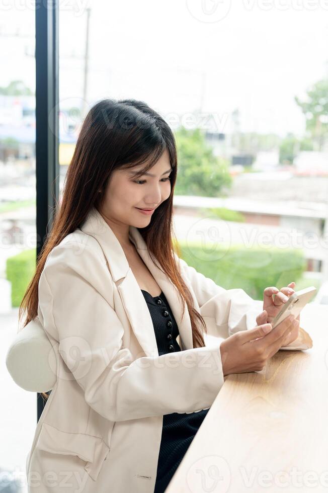 A businesswoman in a white suit is relaxing in a cafe, having a coffee and using her smartphone. photo