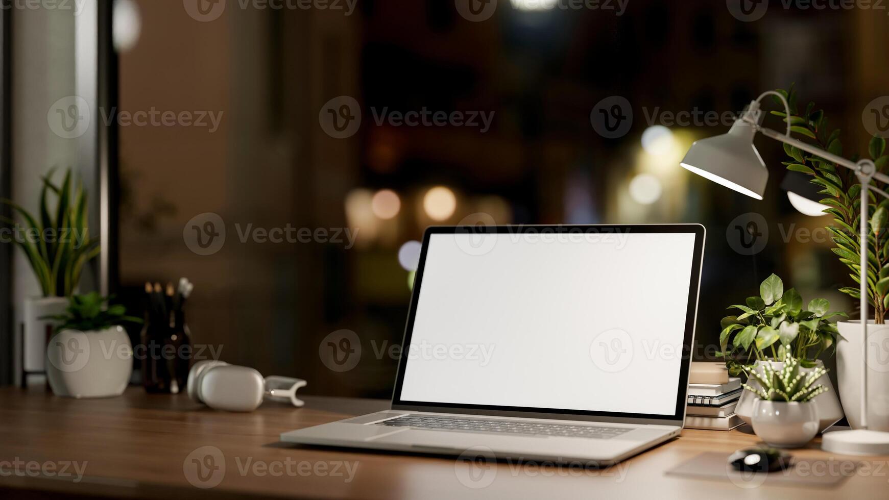 A laptop computer with a white-screen mockup on a wooden table in a dark room at night. photo
