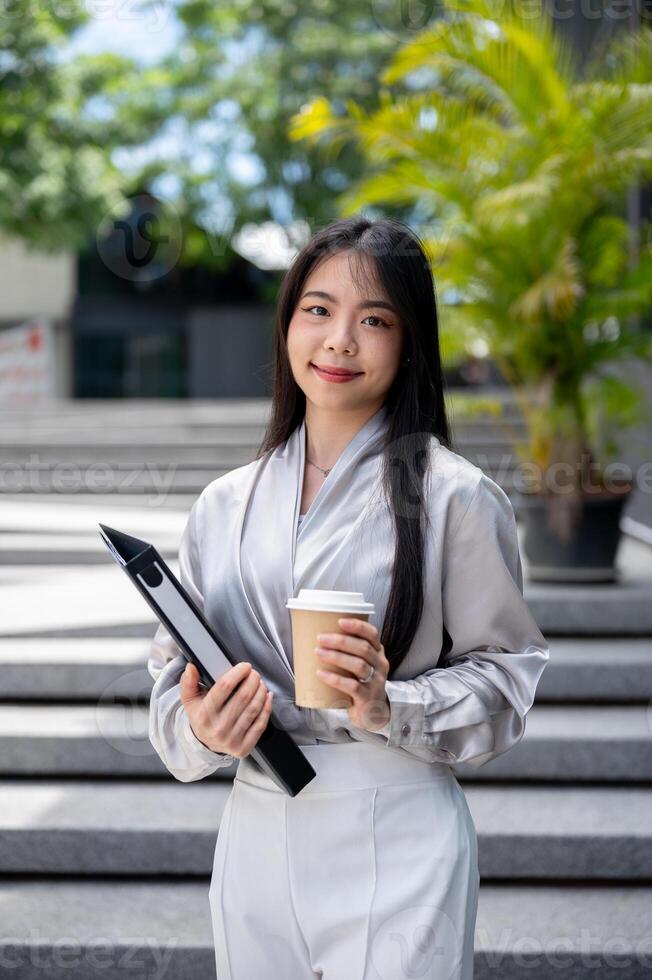 Attractive Asian businesswoman with a file folder and a coffee cup, standing on the stairs outdoors. photo