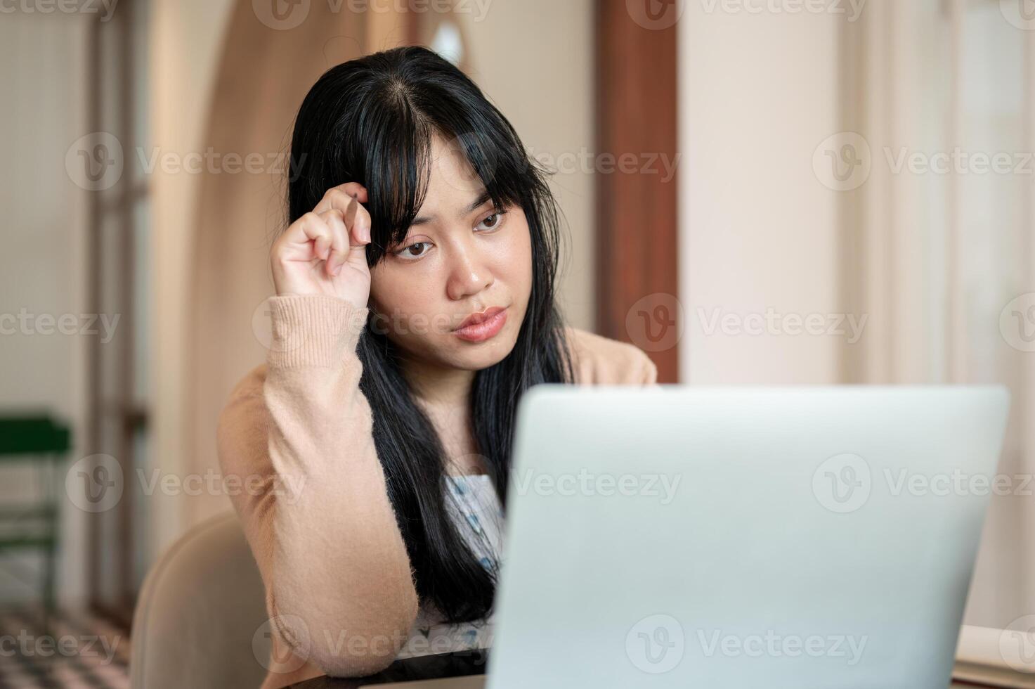 A serious, thoughtful Asian woman is focusing on working on her laptop computer, at a coffee shop. photo