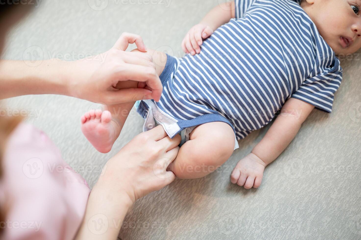 A close-up image of a caring mom is putting clothes on her newborn baby son on the sofa. photo