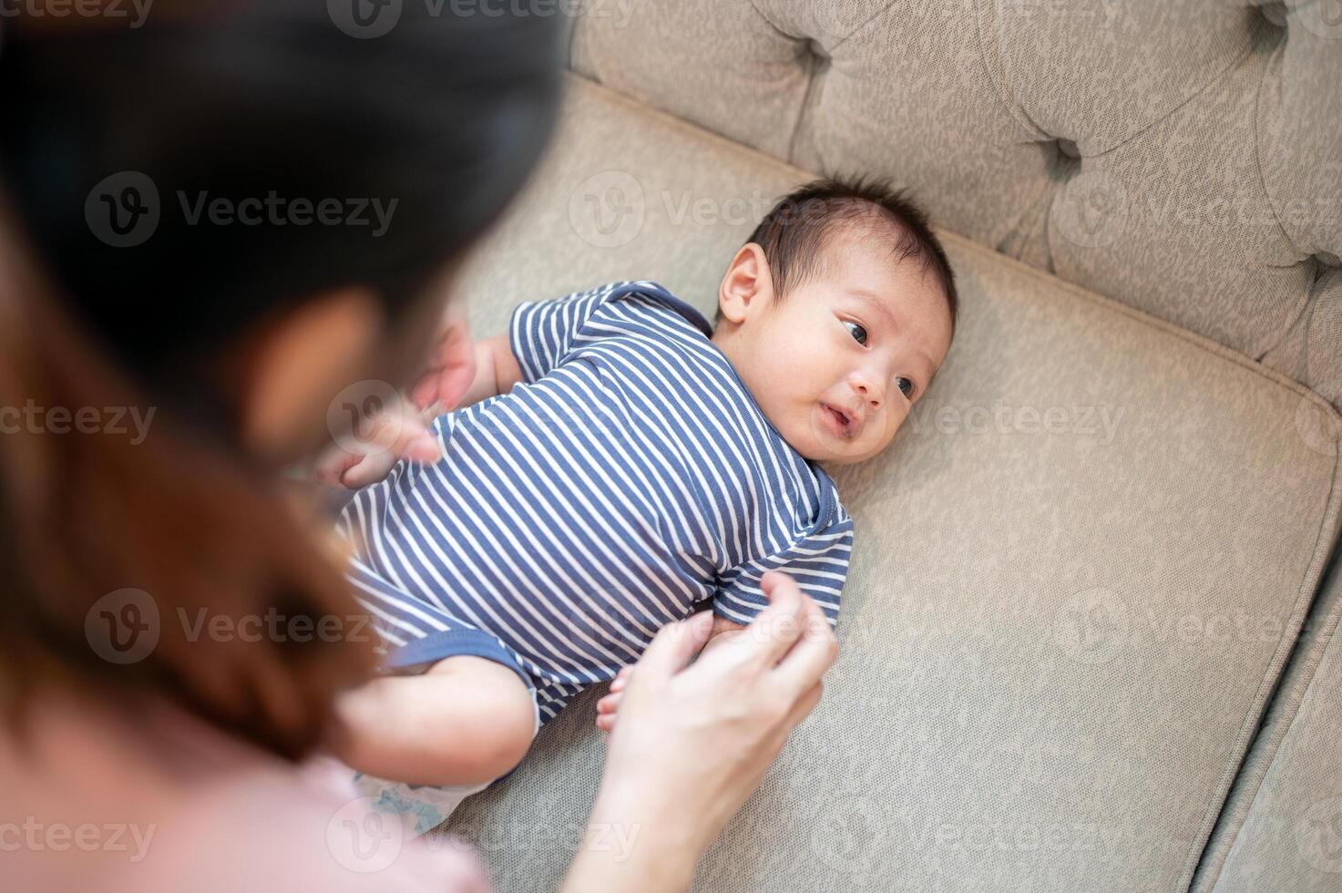 A close-up image of a caring mom is putting clothes on her newborn baby son on the sofa. photo