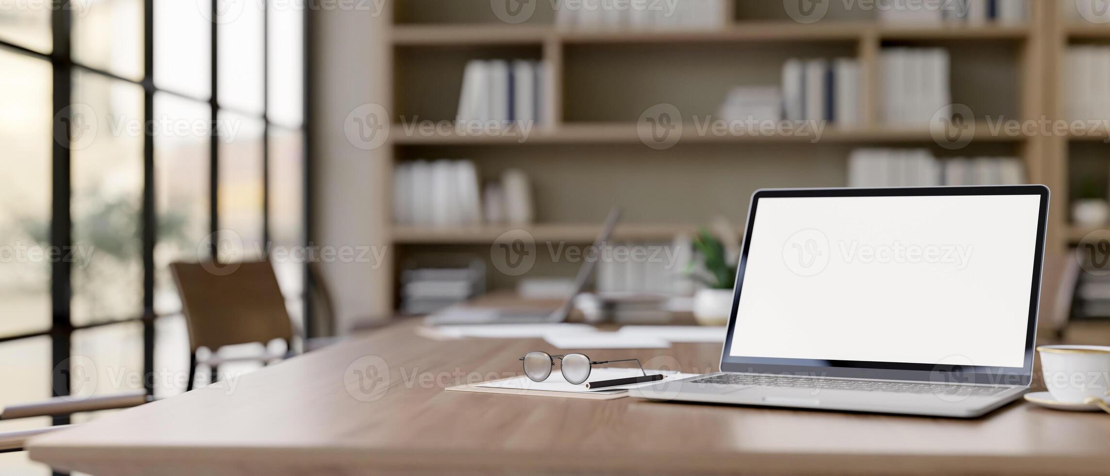 A laptop computer with a white-screen mockup on a wood meeting table in a contemporary meeting room. photo