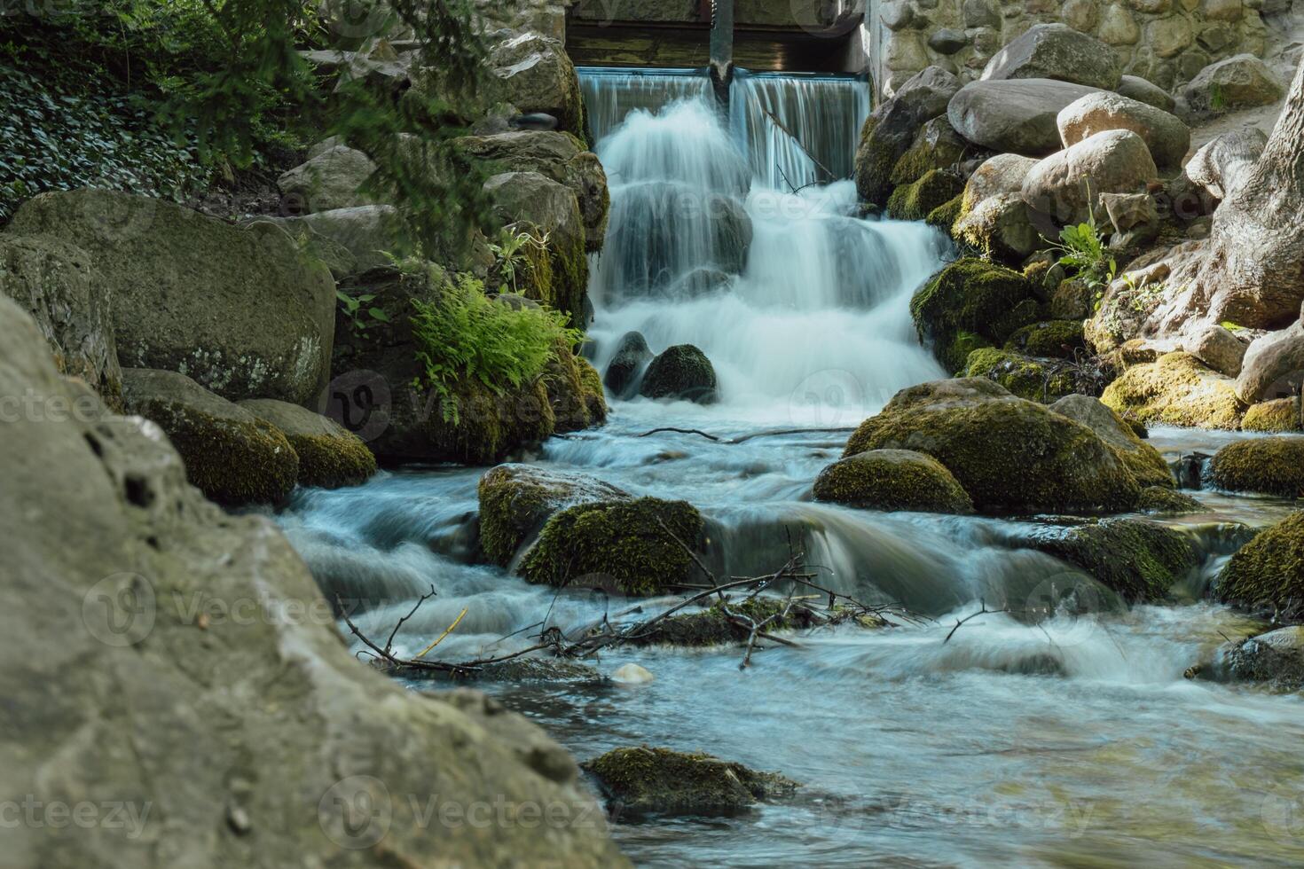 Waterfall cascade in Olivia public park Gdansk Poland. River waterfall falls from cliff and trees. Tourist attraction with small waterfall and clear water Long exposure Unity with nature photo