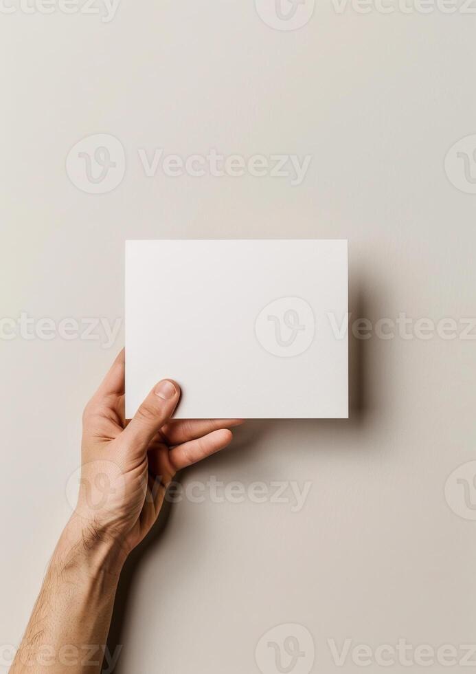 Hand holding blank white card against beige background. Ideal for mockups, business presentations, invitations, or greeting card designs. photo