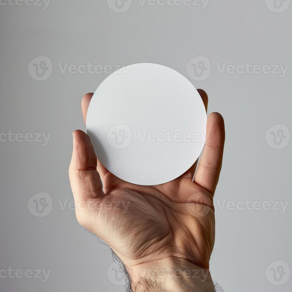 Hand holding a blank white circle card against a neutral background for copy space and design mockup. photo