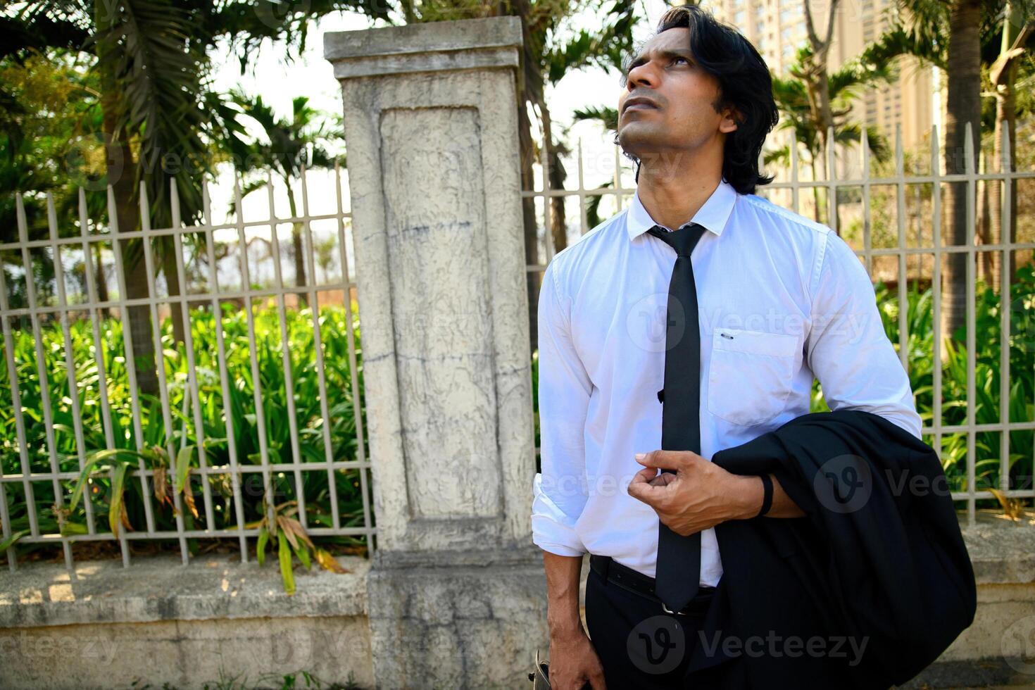 Man holding a black jacket and looking up photo