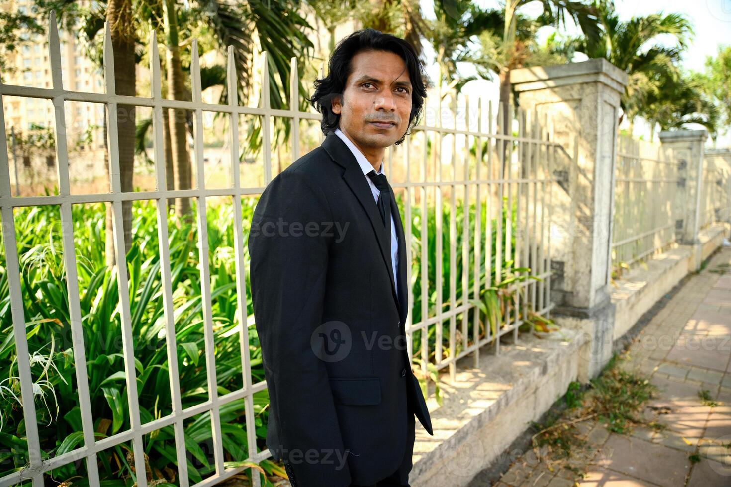 Smiling man in suit standing by a fence photo
