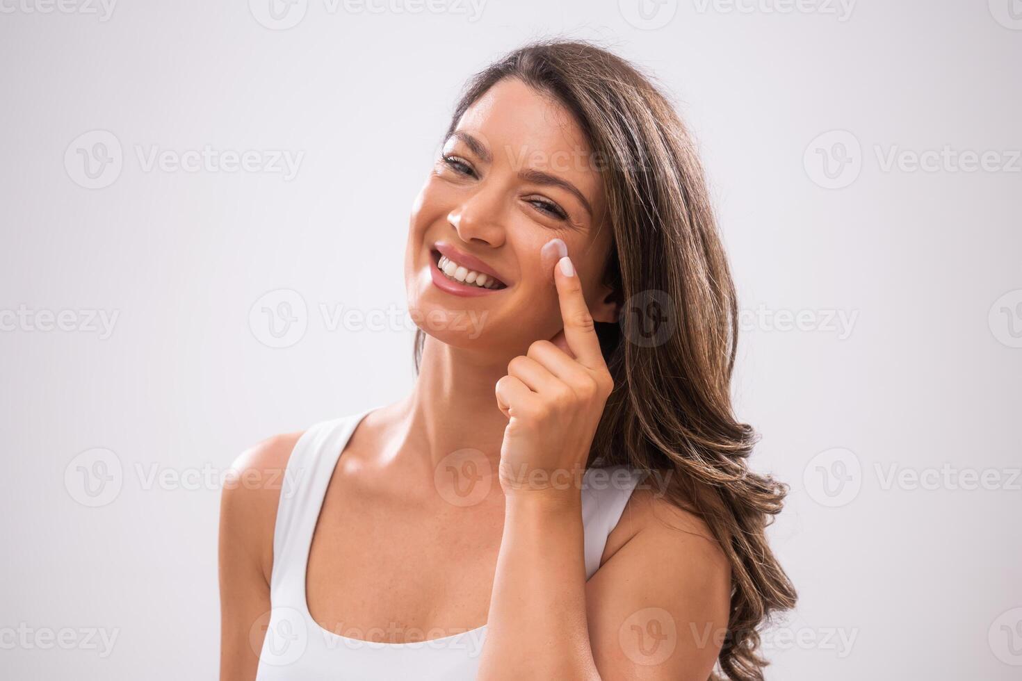 Portrait of adult woman who is applying skin cream on her face. photo