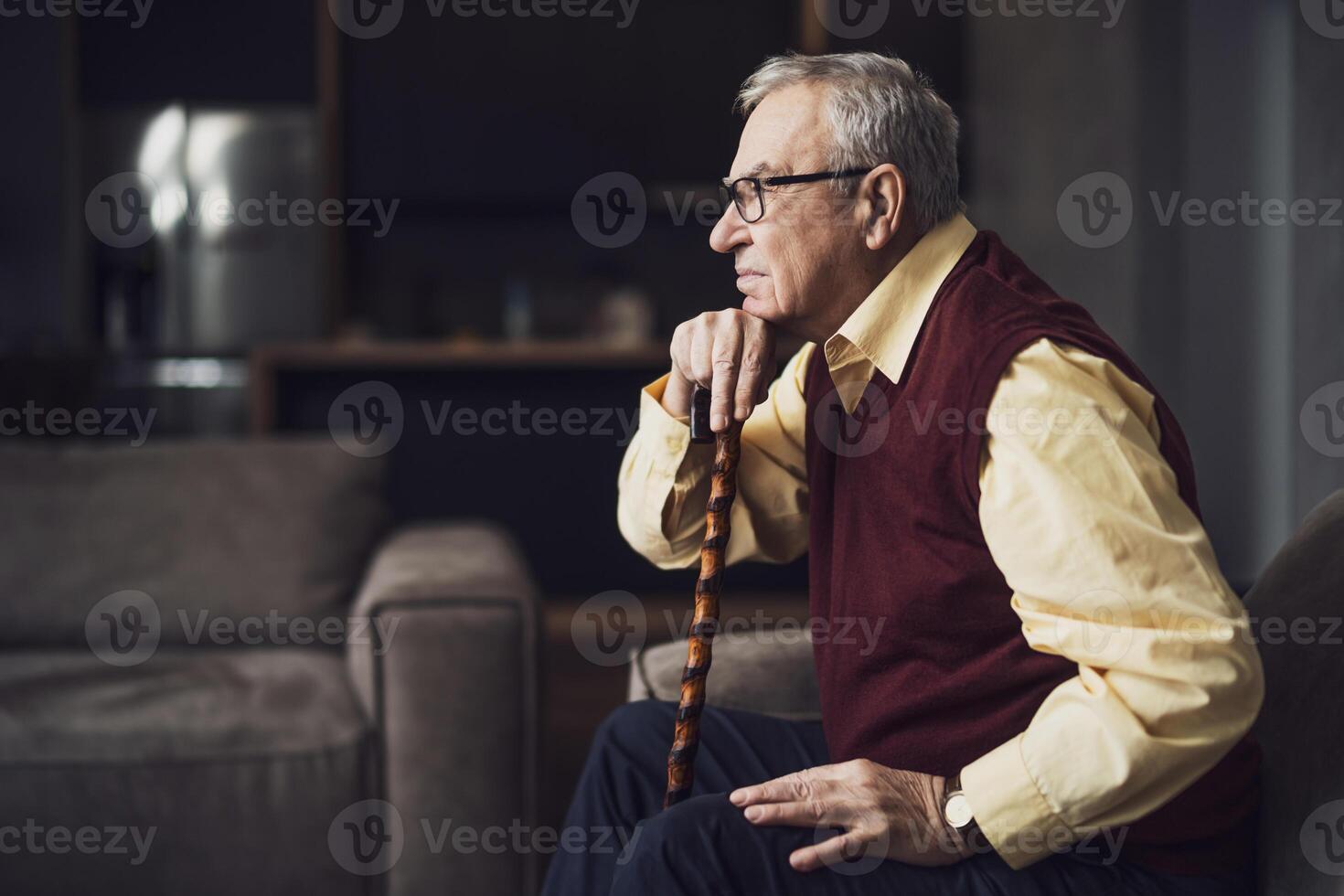 Pensive and worried senior man is sitting on bed in his home. Portrait of senior man with walking cane. photo