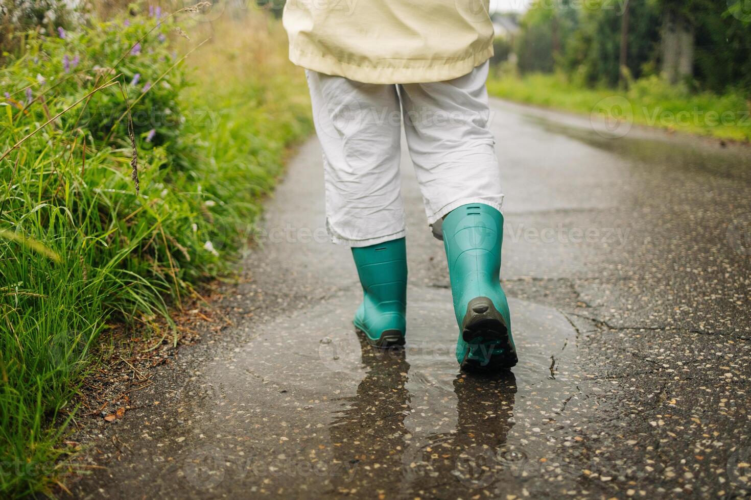 Woman wearing rain rubber boots walking running and jumping into puddle with water splash and drops in autumn rain. photo
