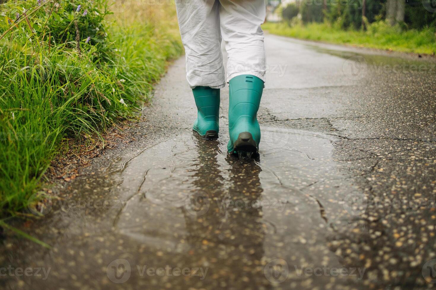 Woman wearing rain rubber boots walking running and jumping into puddle with water splash and drops in autumn rain. photo