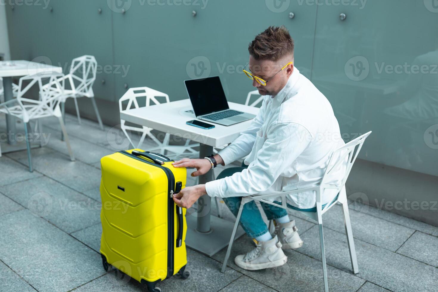 Happy traveling Caucasian man in stylish clothes uses mobile smartphone and laptop, checking trip destination on Internet. Male waiting at flight gates for plane boarding, smiling have a vacation trip photo