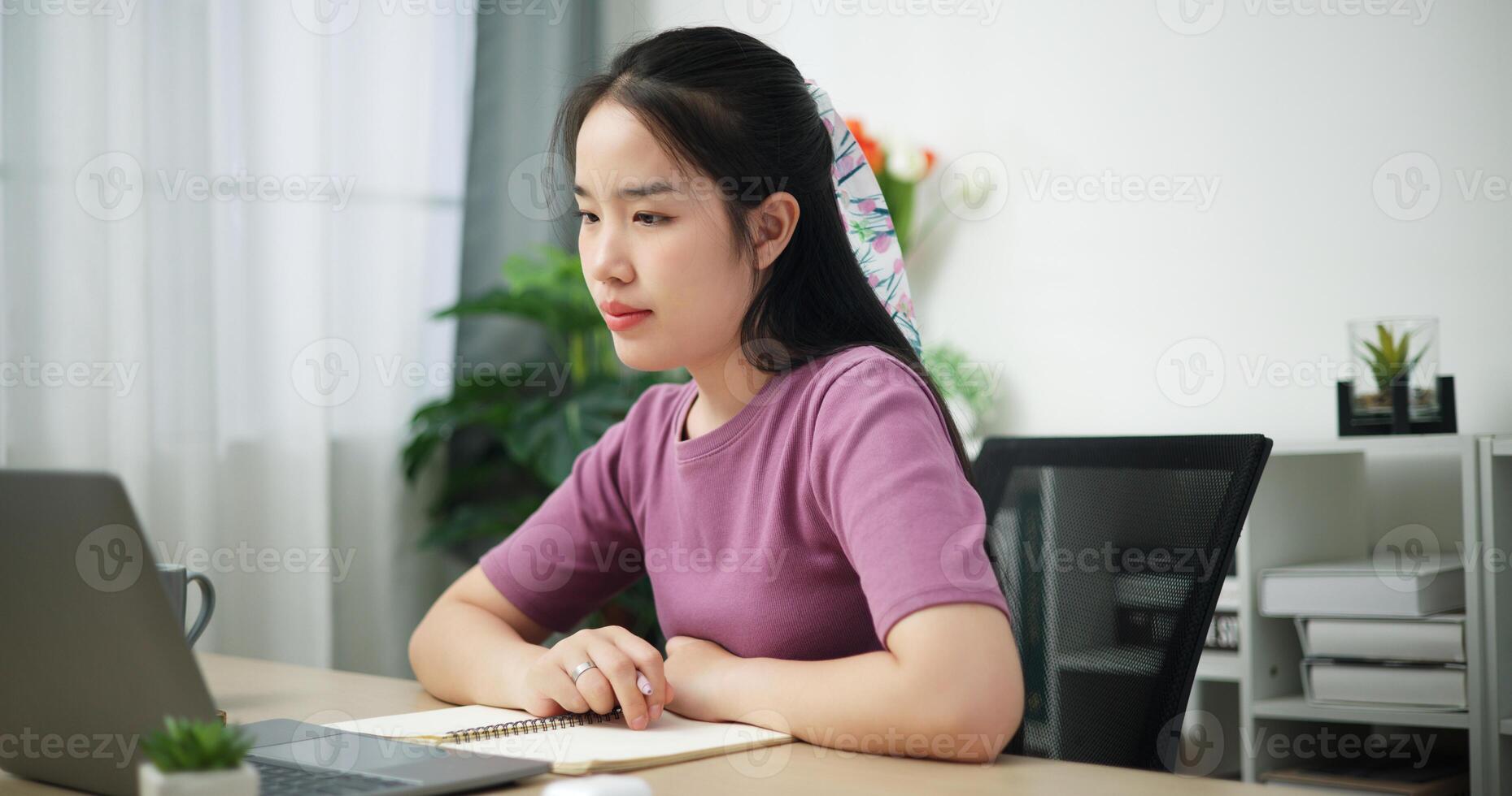 Portrait of Young Asian businesswoman having a conference on digital tablet and write notes in a notebook at home office, online meeting for remote work photo