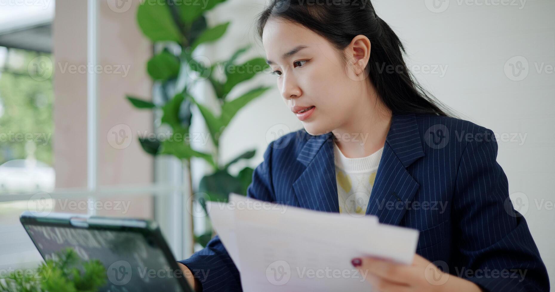 Portrait of Asian businesswoman in suit use digital tablet for work and analyze documents in small coffee shop. Work from anywhere, Remote working photo