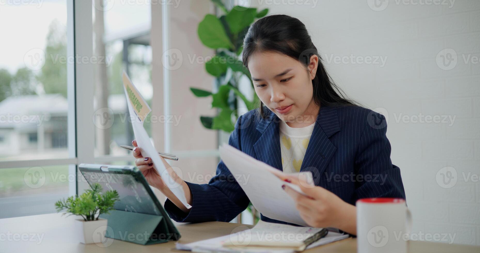 Portrait of Asian businesswoman in suit use digital tablet for work and analyze documents in small coffee shop. Work from anywhere, Remote working photo