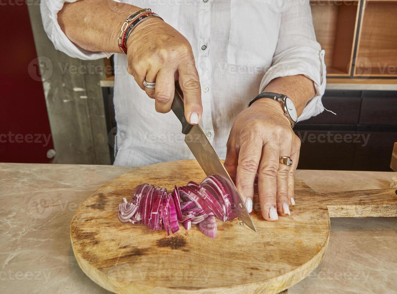 A woman cuts purple onions on a wooden board in her home kitchen photo