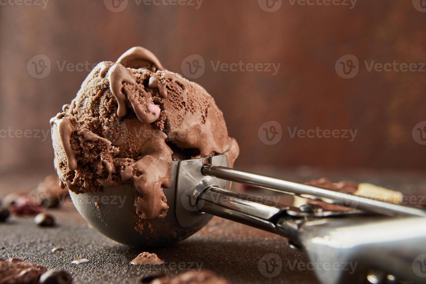 Chocolate ice cream in special metal spoon for rolling balls on brown concrete background photo