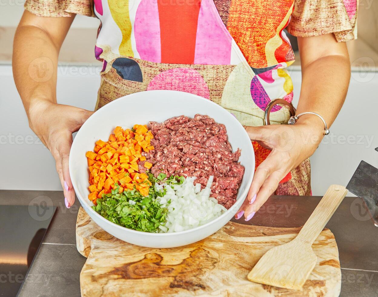 Close-up of a woman holding a bowl of fresh minced meat, vegetables and herbs in the kitchen. photo
