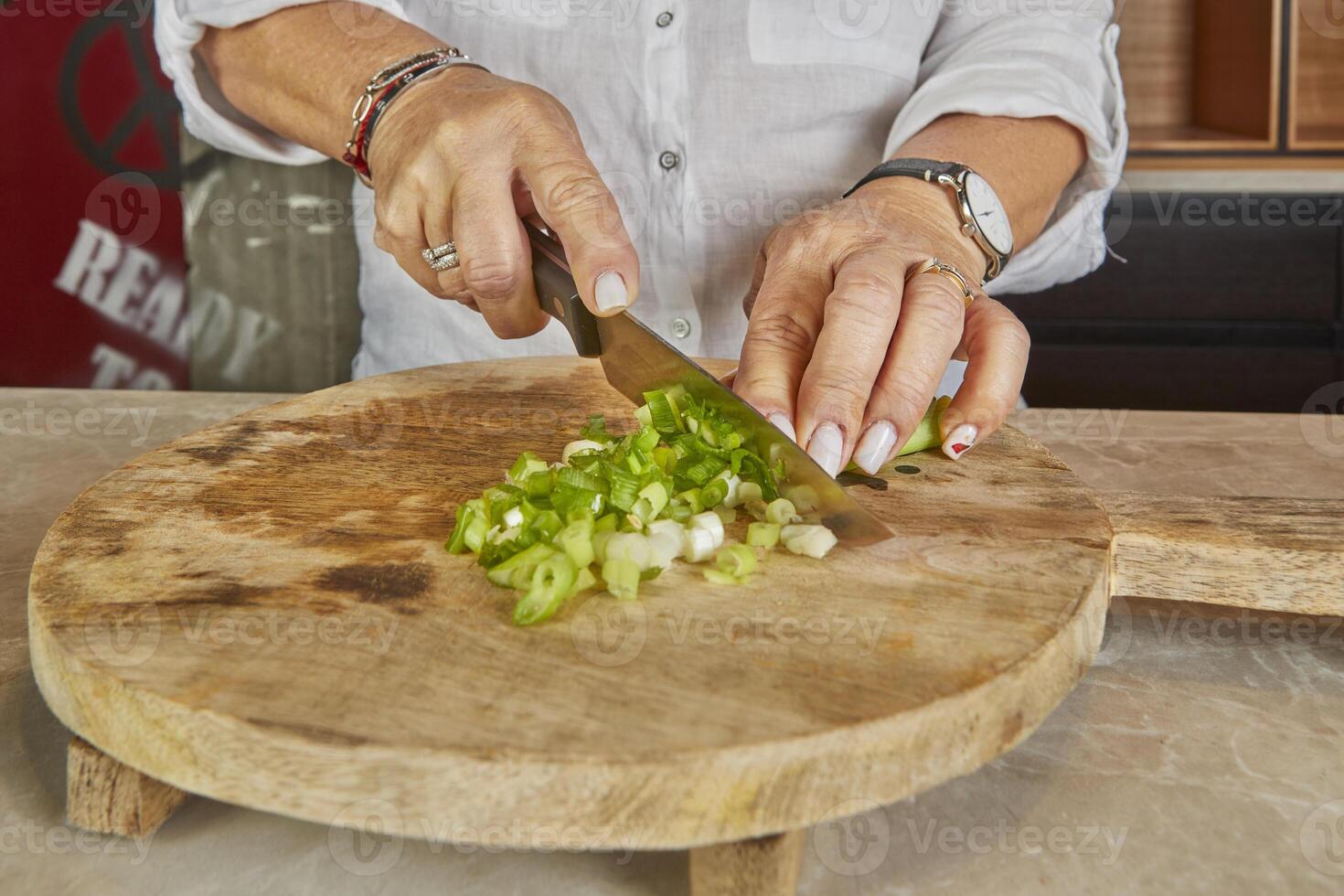 A woman chops green onions on a wooden board in her home kitchen photo