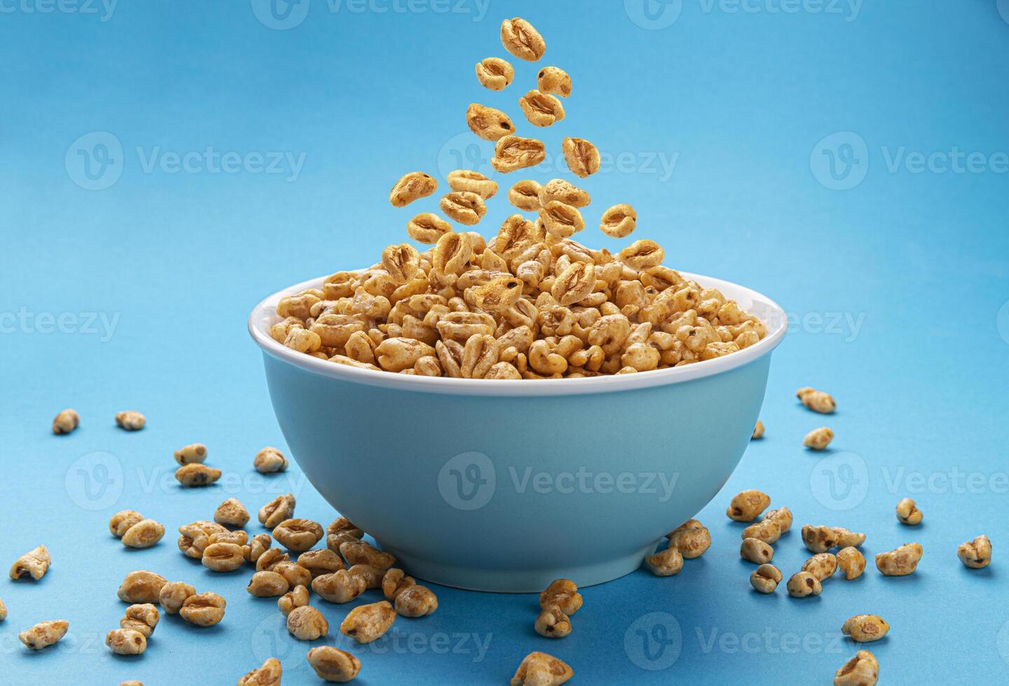 Falling puffed wheat cereal in bowl on blue background photo
