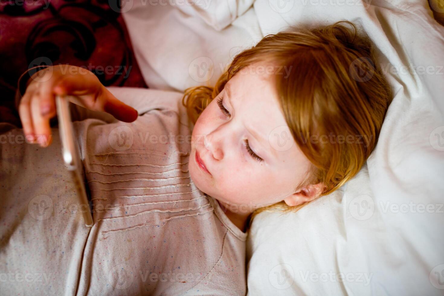 Little girl lying in bed with a thermometer in her mouth. photo